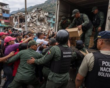 Imagen editorial de fuerzas de seguridad controlando suministros humanitarios frente a una multitud de civiles en una zona urbana afectada por un terremoto, utilizada para ilustrar denuncias sobre desvío de ayuda y obstáculos al rescate en Venezuela.