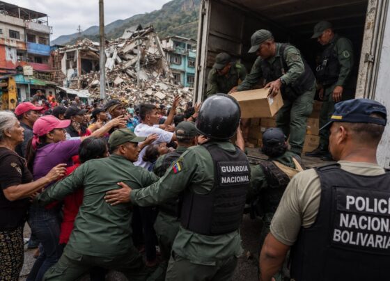 Imagen editorial de fuerzas de seguridad controlando suministros humanitarios frente a una multitud de civiles en una zona urbana afectada por un terremoto, utilizada para ilustrar denuncias sobre desvío de ayuda y obstáculos al rescate en Venezuela.